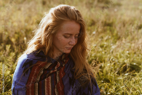 on the steppe grass sits a blond girl with long hair in an ethno cape and something is considering. High quality photo