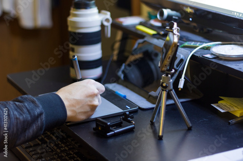A person's hand holding a pen and using a graphic tablet with a mini phone tripod at a home setup for a content creator.