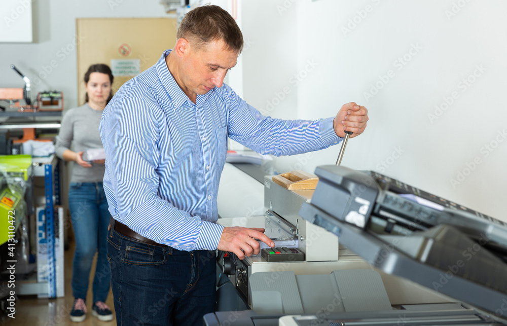 Obraz premium Worker of printing with a stack of paper at the machine, in a printing factory. High quality photo