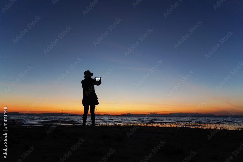 The silhouette of a girl holding a phone in hand to take a morning view