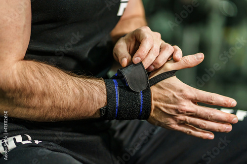 Close up on hands of unknown man holding and putting on and adjusting wrap bandages on wrists for powerlifting body building training sport equipment at the gym