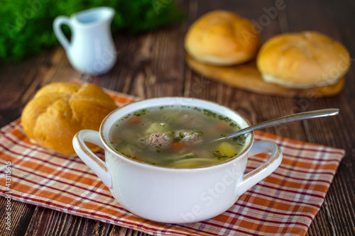 Hot soup with meatballs and vegetables in a wooden bowl on a wooden table. 