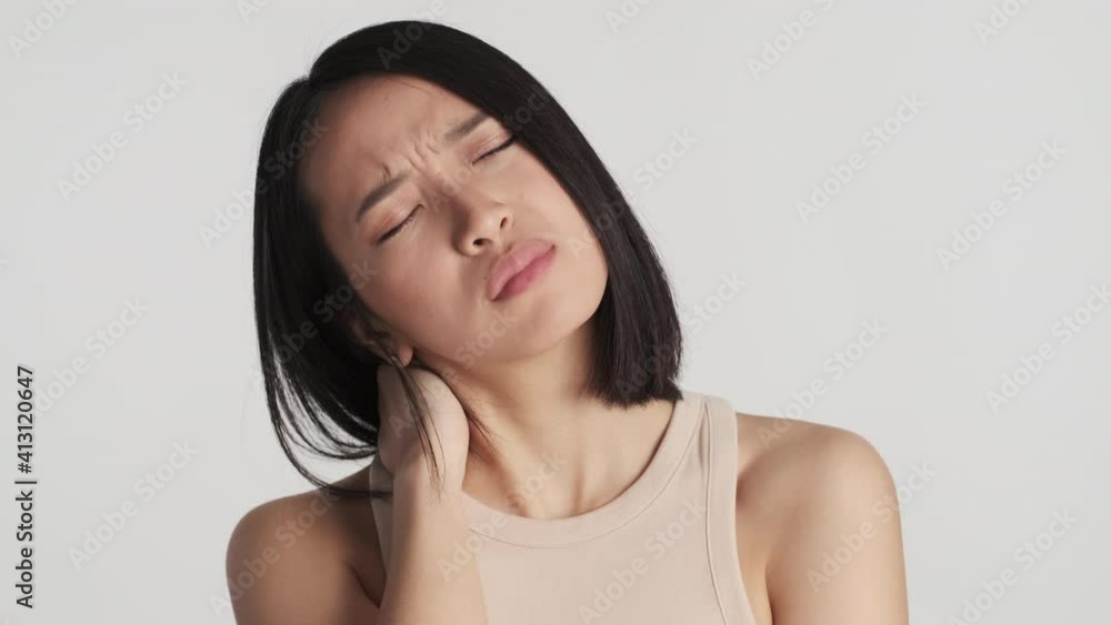 Young beautiful tired Asian woman feeling pain in neck and head after hard day posing over white background. Overworked expression Young beautiful tired Asian woman feeling pain in neck and head after hard day posing over white background. Overworked expression