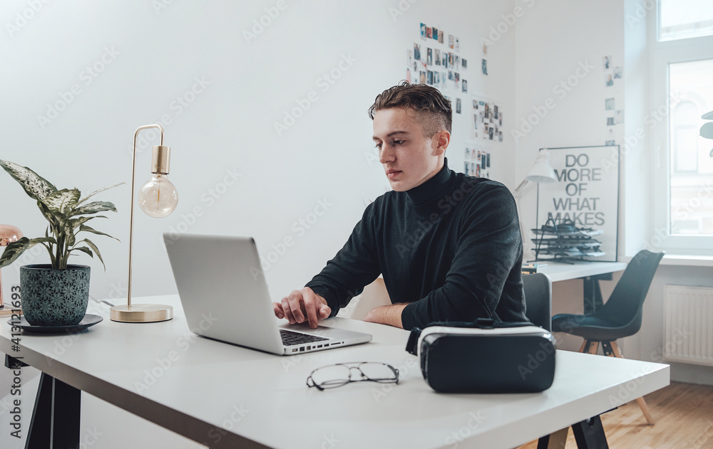 Stylish businessman in black sweater works on modern laptop sitting at table in comfortable office room. Stylish businessman in black sweater works on modern laptop sitting at table in comfortable office room.