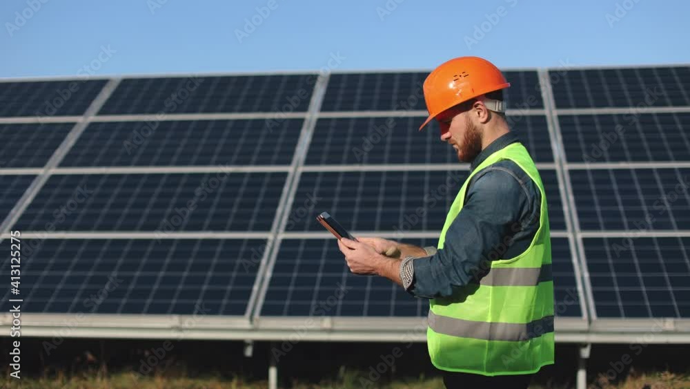 The engineer is entering the data into the tablet. He is standing next to solar panels. 4K. The engineer is entering the data into the tablet. He is standing next to solar panels. 4K.