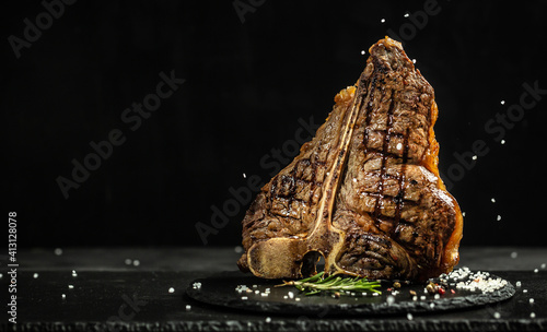 Grilled Premium Dry Aged T-bone Steak or porterhouse steak adding salt in a freeze motion on black background. USDA Prime Beef. Restaurant menu, cookbook recipe. Long banner format