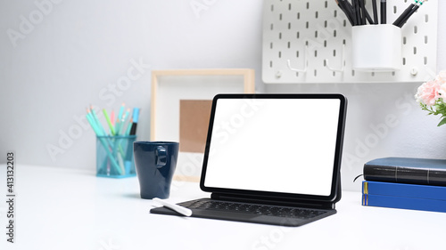 Designer workplace with computer tablet, coffee cup, books and stationery on white table.