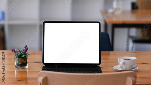 Front view of tablet computer with blank screen, coffee cup and plant on wooden desk.
