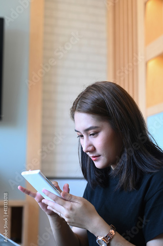 Portrait of smiling young female sitting in modern offie and using mobile phone.