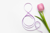 Figure 8 made of violet ribbon and tulip flower on light background. International Women's Day celebration