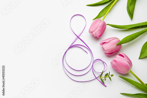 Figure 8 made of violet ribbon and tulip flowers on light background. International Women's Day celebration