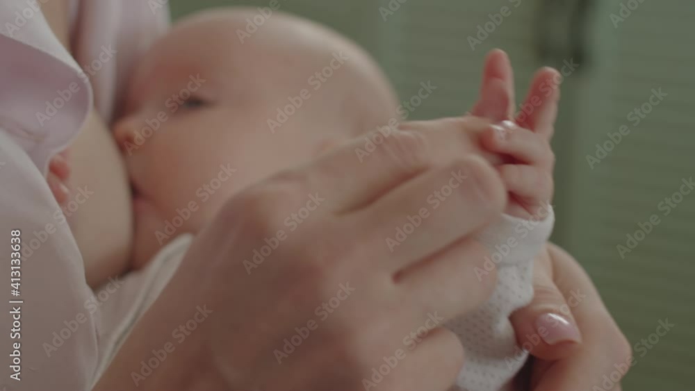 Close up shot of loving mother touching tiny hand of baby daughter while breastfeeding her at home Close up shot of loving mother touching tiny hand of baby daughter while breastfeeding her at home