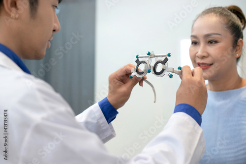 Optometrist with trial frame checking senior Asian woman patient vision at ophthalmology clinic, selective focus