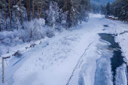 View of almost frozen Sema river and tourist camping on its bank. Kamlak village, Altai Republic, Russia.