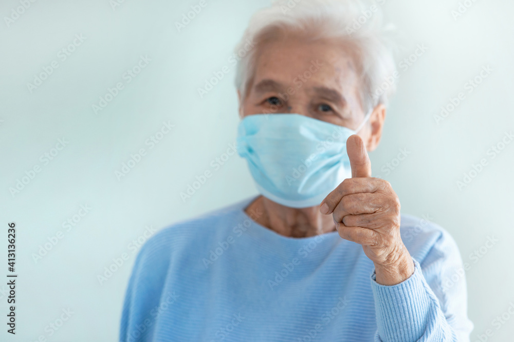 Asian granny woman wear a medical mask, gray haired elderly woman in protective mask and showing thumb up OK sign Asian granny woman wear a medical mask, gray haired elderly woman in protective mask and showing thumb up OK sign