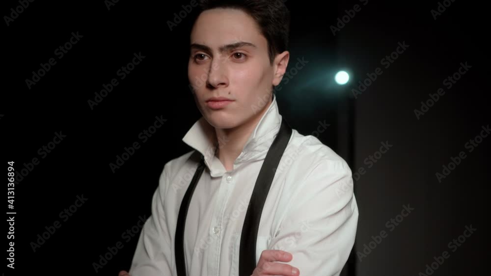 Pensive young man in a dark room. Portrait of a serious guy in a white shirt who crossed his arms. Inner calmness and self-confidence. Pensive young man in a dark room. Portrait of a serious guy in a white shirt who crossed his arms. Inner calmness and self-confidence.