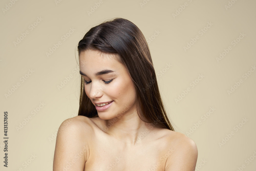 Obraz premium Woman with bared shoulders dark hair clean skin makeup beige background