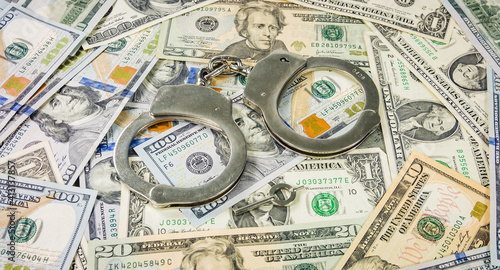 Steel police handcuffs lying on the american dollars banknotes. Close-up photo