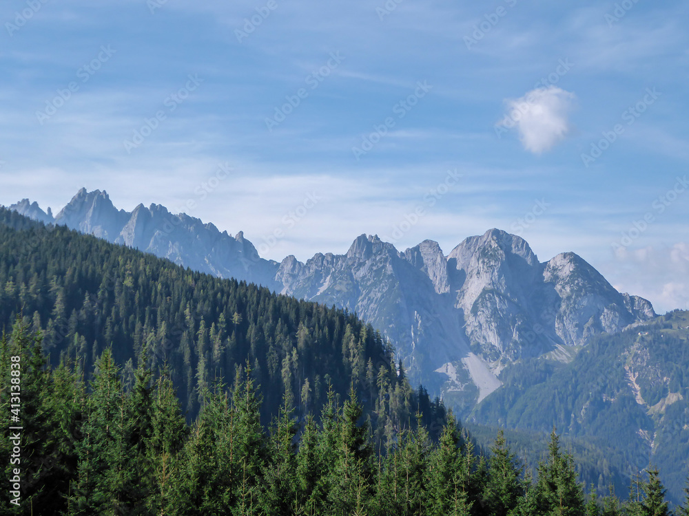A panoramic view on high Alps in the region of Gosau, Austria. The lower mountains are overgrown with dense forest. The chains in the back are stony and barren. Clear, sunny day.