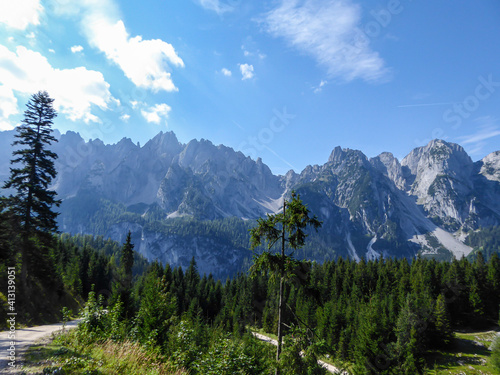 Gravelled road in the mountains with the view on high Alps in the region of Gosau, Austria. The lower mountains are overgrown with dense forest. The chains in the back are stony and barren. Sunny day