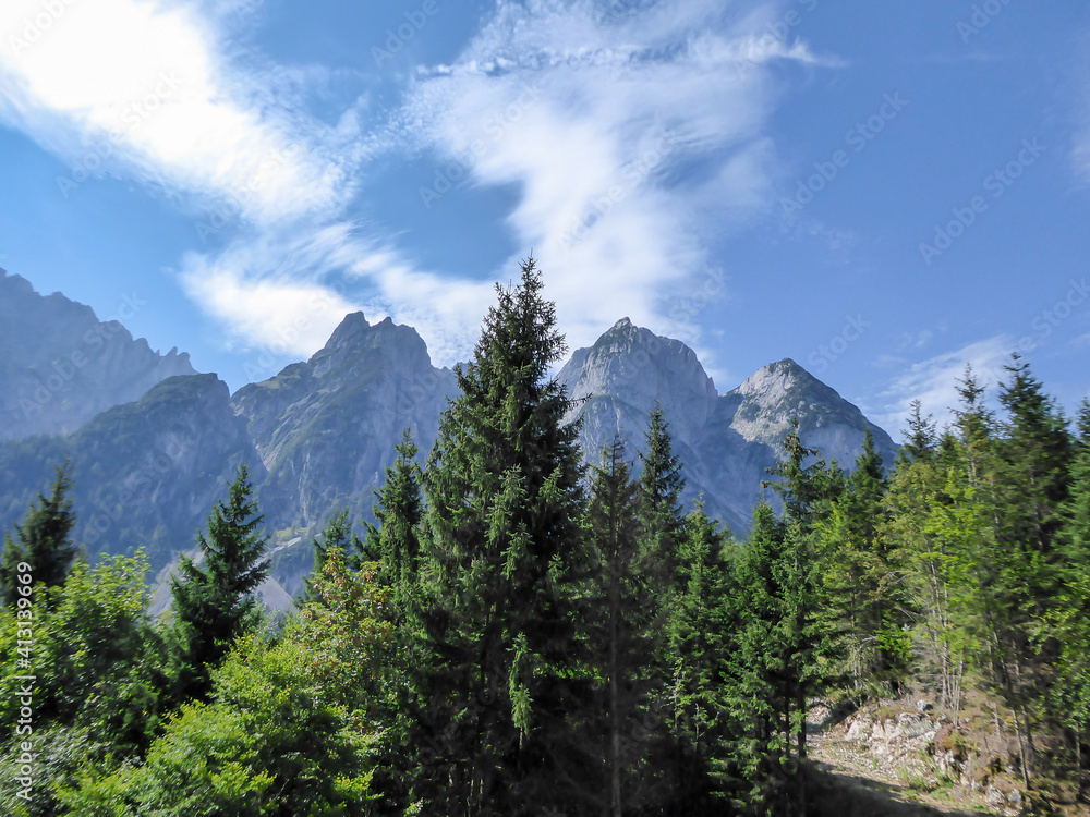 Gravelled road in the mountains with the view on high Alps in the region of Gosau, Austria. The lower mountains are overgrown with dense forest. The chains in the back are stony and barren. Sunny day