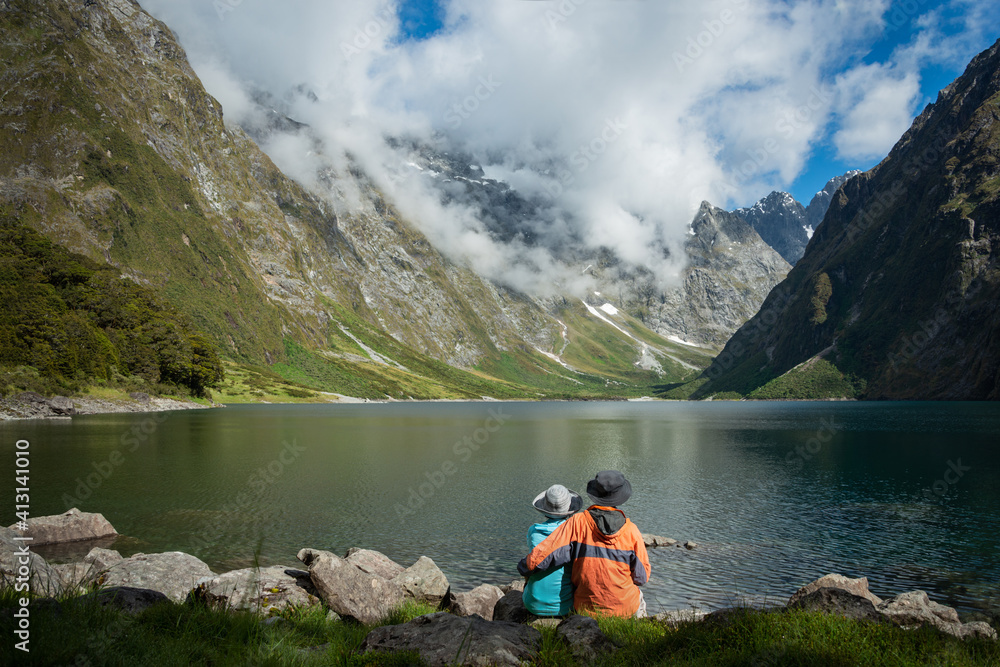 A Couple sitting on the shore of Lake Marian, enjoying the views, Fiordland National Park, New Zealand