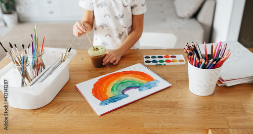 Kids painting watercolor rainbows at table at home