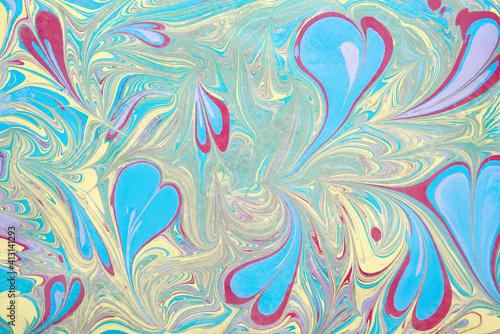An illustration in the art of an ebru with multicolored hearts of liquid acrylic paint spreading over paper. Bright pastel colors