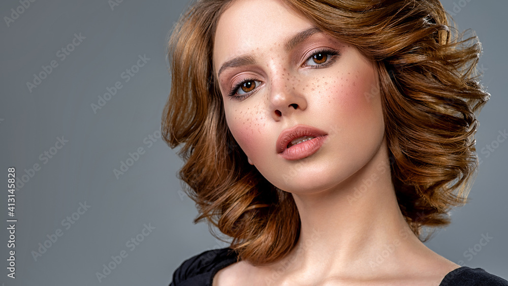 Fototapeta premium Woman with a curly hair. Beautiful young woman with freckles on face. Beautiful brown haired with stylish short hairstyle. Closeup portrait of an attractive girl with a brown makeup.