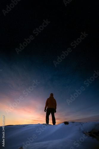 Low angle view of a man looking at the sunset in winter with stars in the sky