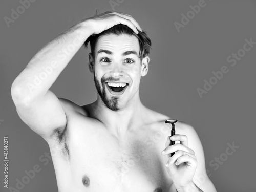 Handsome man with half shaven face chin and beard, moustache holding safety razor with naked chest on green background. Male beauty, skincare, hygiene.