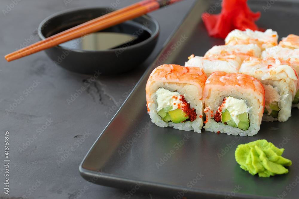 Sushi roll covered with shrimp meat on black ceramic plate Sushi roll covered with shrimp meat on black ceramic plate