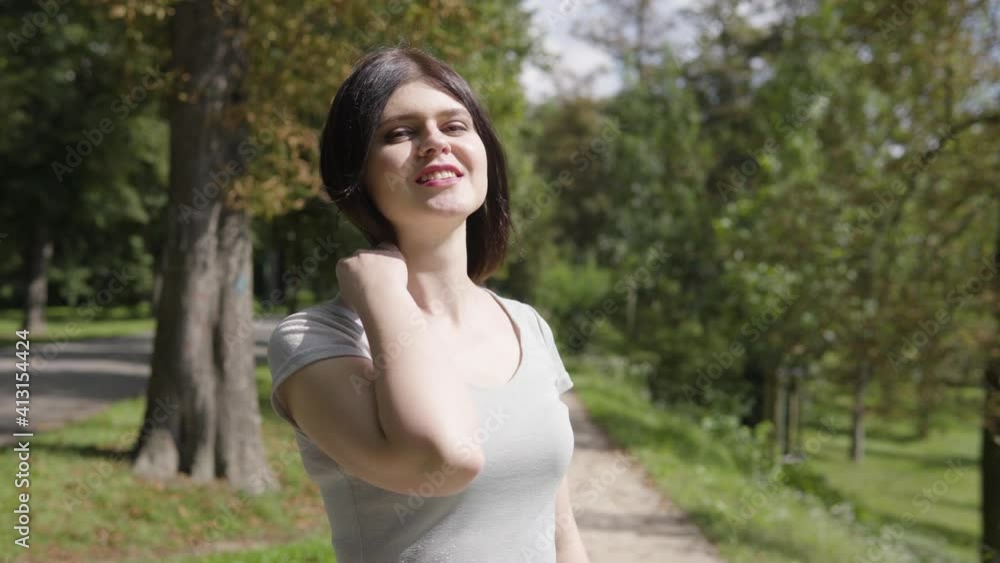 A young Caucasian woman smiles at the camera on a pathway in a park on a sunny day A young Caucasian woman smiles at the camera on a pathway in a park on a sunny day
