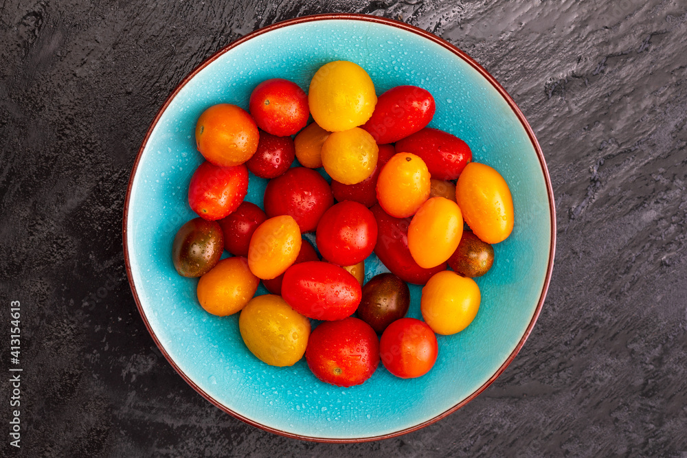 Bowl of colorful cherry tomatoes (red, garnet and yellow), fresh and raw. With water drops. On black textured background and space to insert text (copy space). Top View Bowl of colorful cherry tomatoes (red, garnet and yellow), fresh and raw. With water drops. On black textured background and space to insert text (copy space). Top View