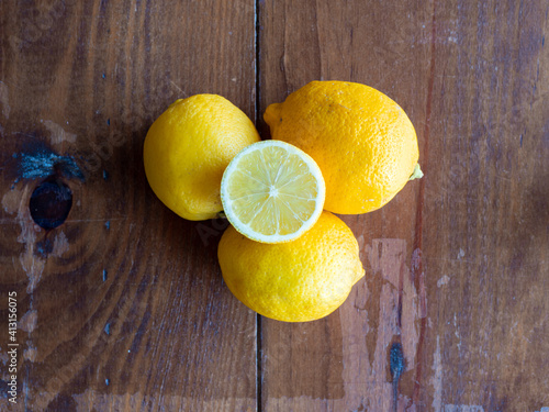 Top view of three lemons on a wooden table with one open on top of them 