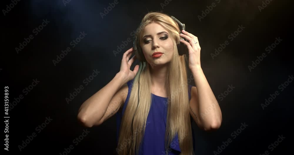 Slow motion fashion portrait of woman dancing in headphones isolated. Pretty lady with long blond hair posing in studio in smoke. Music, glamour lifestyle concept. happy female listening to songs. Slow motion fashion portrait of woman dancing in headphones isolated. Pretty lady with long blond hair posing in studio in smoke. Music, glamour lifestyle concept. happy female listening to songs.