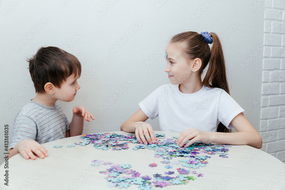 Happy boy and a girl collect a puzzle sitting at a table Happy boy and a girl collect a puzzle sitting at a table