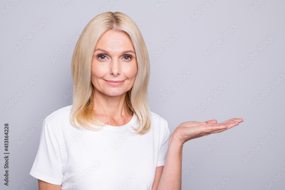 Photo portrait of elderly lady holding blank space in one hand isolated on grey colored background Photo portrait of elderly lady holding blank space in one hand isolated on grey colored background