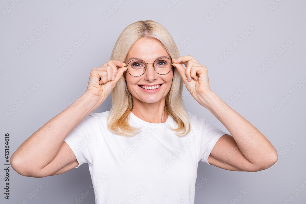 Photo portrait of old woman touching glasses with two hands isolated on grey colored background Photo portrait of old woman touching glasses with two hands isolated on grey colored background