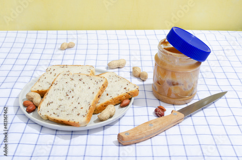 Сloseup of plate full of slices of bread with flax seeds, peanuts, jar of peanut butter, knige on the tablecloth photo