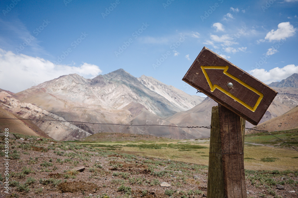 Directional sign with arrow on wooden plank pointing to sky. Arid mountains landscape. Aconcagua National Park, Andes Mountains, Argentina
