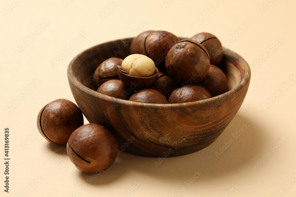 Bowl with tasty macadamia nuts on beige background Bowl with tasty macadamia nuts on beige background