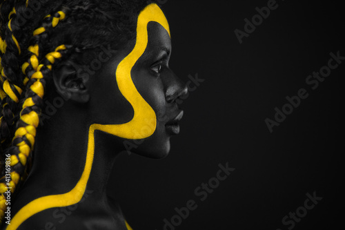 Yellow and black body paint. Woman with face art. Young girl with colorful  bodypaint. An amazing afro american model with makeup. Stock Photo