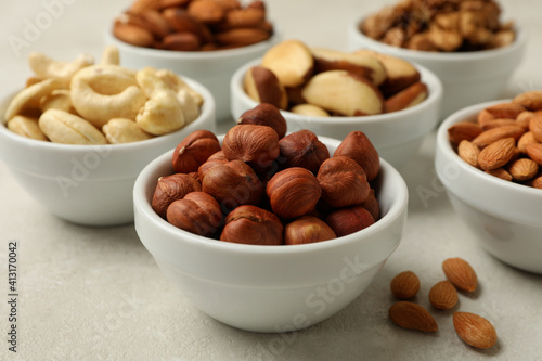 Bowls with different nuts on white textured background, close up