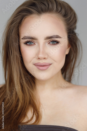 A beautiful female model with fresh daily makeup and a romantic look. Vertical photo with a close-up of the girl's face.