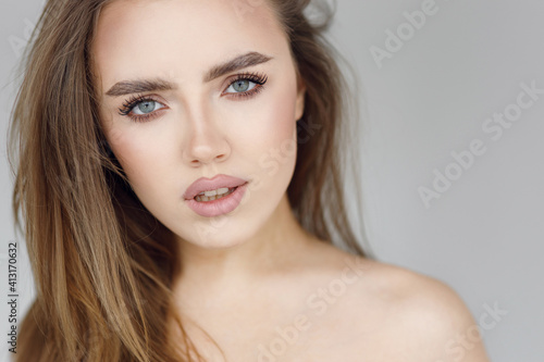 The face of a young beautiful girl with natural makeup  beauty portrait. Clear skin and an expressive look on the girl s face  on a gray background.