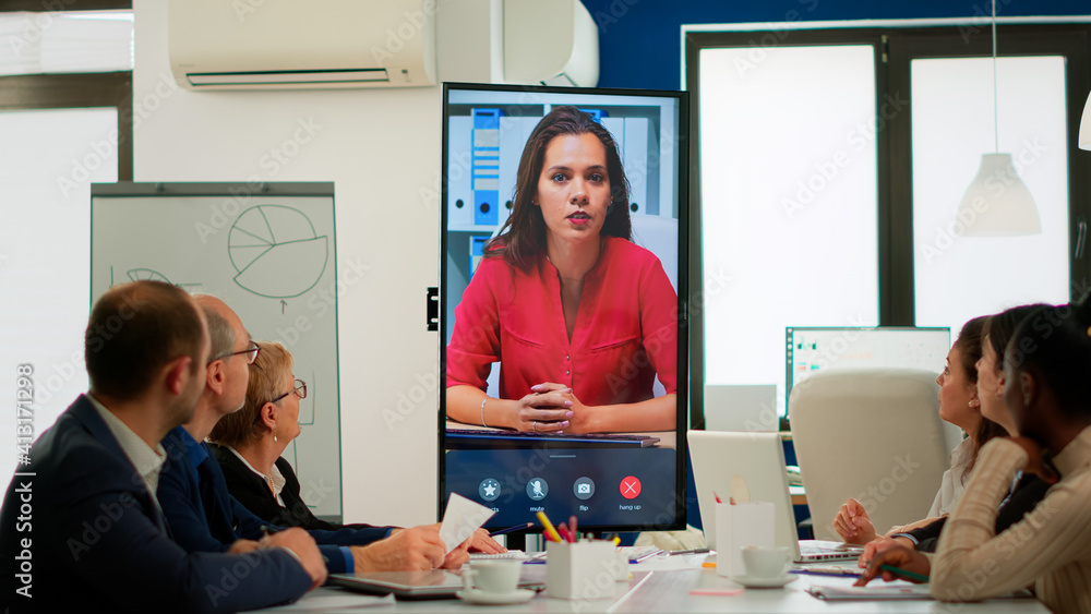 Obraz premium Diverse executive team meeting at conference video call looking at huge display. Business people talking to webcam, do online conference participate internet brainstorming, distance office discussion