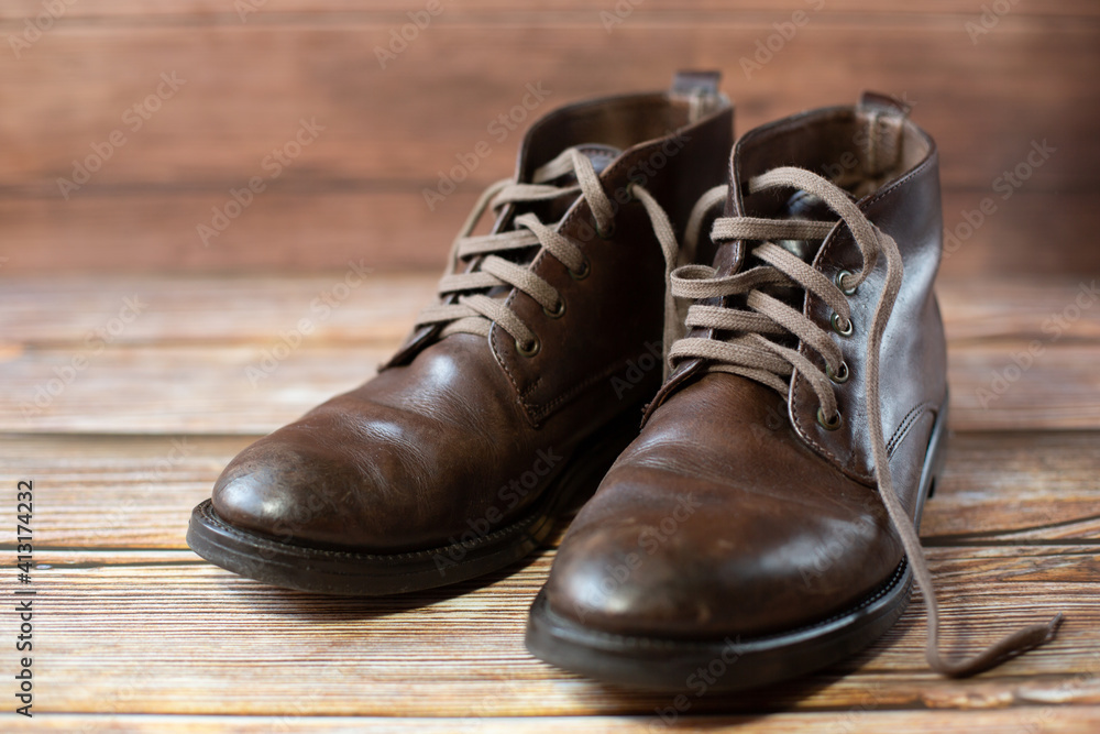 A pair of mens worn brown leather shoes with laces in a retro style stand on a wooden background. A pair of mens worn brown leather shoes with laces in a retro style stand on a wooden background.