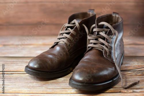 A pair of mens worn brown leather shoes with laces in a retro style stand on a wooden background.