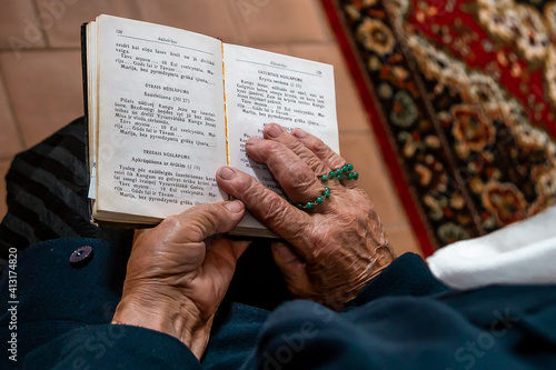 Close up of an old woman holding hands open bible and rosary and praying